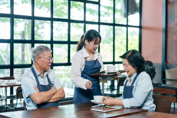Senior asian couple restaurant owners wearing apron receiving coffee from young waitress smiling...