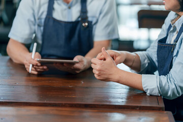 Elderly asian couple in aprons discussing cafe finances using tablet teamwork cooperation small...