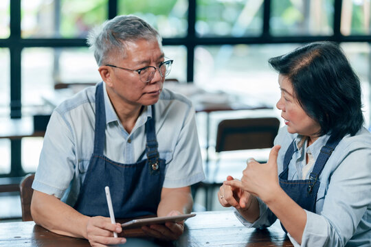 Elderly asian couple discussing restaurant performance and financial results using tablet teamwork collaboration communication planning small business management cooperation partnership cafe lifestyle