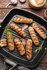 Pan with grilled sausages and spices on wooden table, flat lay