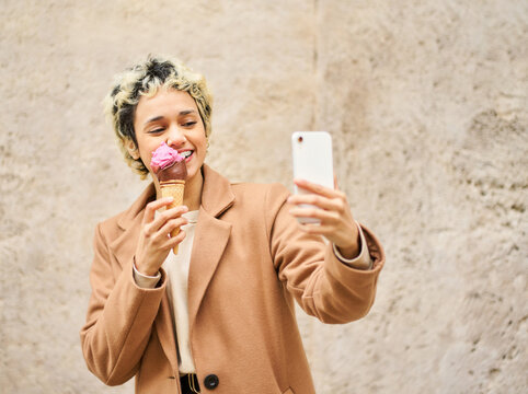 Woman enjoying ice cream and taking selfie outdoors - Powered by Adobe