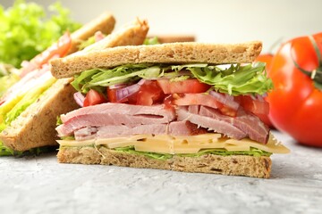 Delicious sandwiches with ham, cheese and vegetables on grey textured table, closeup