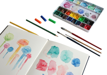 Art supplies and a sketchbook with watercolor paintings are arranged on a black surface.