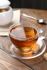 Aromatic black tea in glass cup and brown sugar on wooden table, closeup