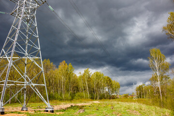 Sturdy electricity pylon commands the foreground, silhouetted against a brooding, stormy sky. Vibrant green spring foliage lines the horizon
