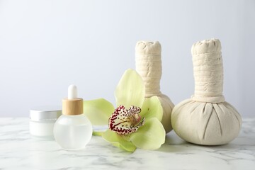 Beautiful spa composition with herbal bags and essential oil on white marble table against light background