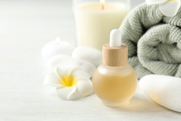 Essential oil, towel, burning candles, plumeria flower and spa stones on white table, closeup. Space for text