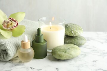Beautiful spa composition with essential oils and burning candle on white marble table, closeup. Space for text