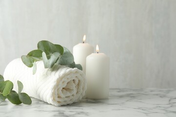 Soft towel, burning candles and eucalyptus leaves on white marble table, closeup. Space for text