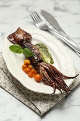 Tasty cooked squid served with sauce, tomatoes, cutlery and basil on white marble table, closeup