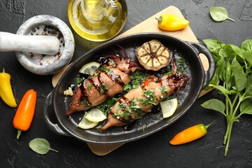 Tasty cooked squids with sauce, garlic and products on black table, flat lay