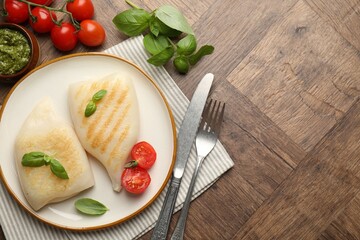 Pieces of tasty grilled squid, tomatoes, basil and sauce on wooden table, flat lay. Space for text