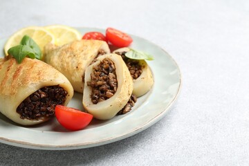 Pieces of tasty grilled squid stuffed with mushrooms, basil, tomatoes and lemon on light grey textured table, closeup. Space for text