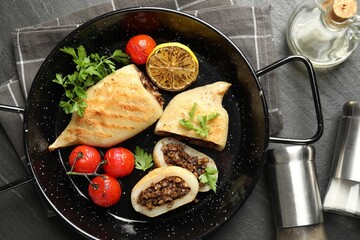 Pieces of tasty grilled squid stuffed with mushrooms, parsley, tomatoes and lemon in pan on dark...