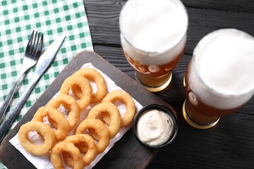 Fried squid rings with sauce and beer served on black wooden table, flat lay
