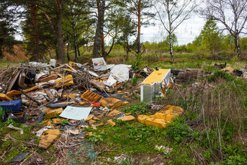 Big illegal trash pile ruins the green forest fringe. Old broken stuff, household junk, and general refuse mess up the natural landscape, showing environmental disrespect
