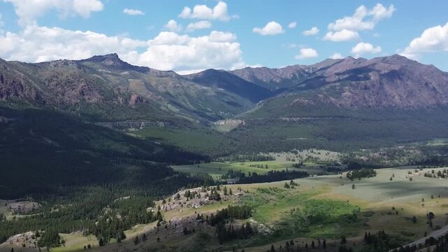 Mountain scenery along the Beartooth Highway in Wyoming. Flying shot pans right to left over a valley towards rugged mountain peaks in the distance.