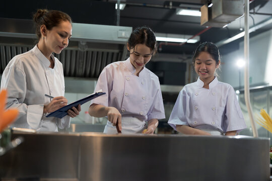 Cooking, Kitchen. Group of young female chef wearing white apron and learning cooking in kitchen at restaurant