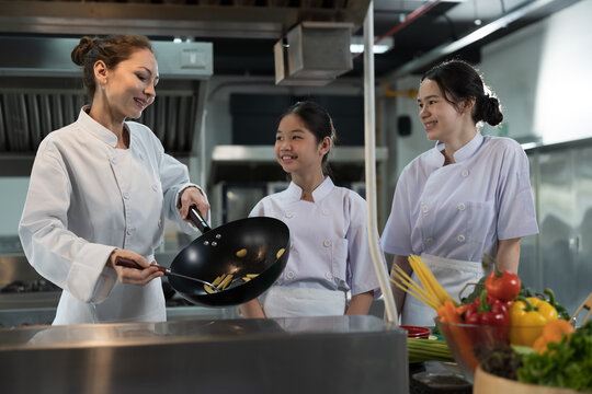 Cooking, Kitchen. Group of young female chef wearing white apron and learning cooking in kitchen at restaurant