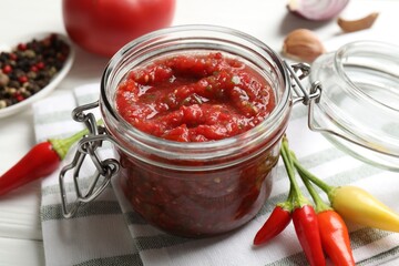 Tasty salsa sauce in jar and ingredients on white wooden table, closeup
