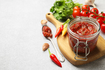 Tasty salsa sauce in jar and ingredients on light table, closeup. Space for text