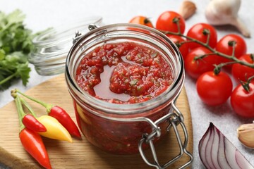 Tasty salsa sauce in jar and ingredients on light table, closeup