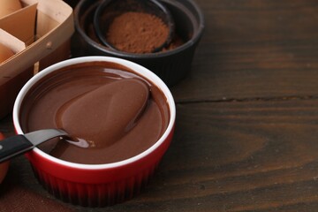 Raw chocolate dough in bowl and ingredients on wooden table, closeup. Space for text