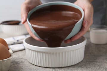 Woman pouring raw chocolate dough into baking dish at grey table, closeup