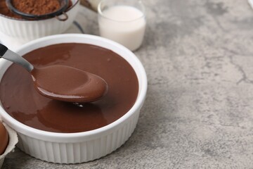 Taking raw chocolate dough from bowl with spoon on grey table, closeup. Space for text