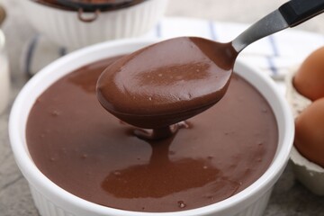 Taking raw chocolate dough from bowl with spoon on grey table, closeup