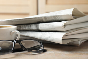 Stack of newspapers, coffee and glasses on wooden table, closeup