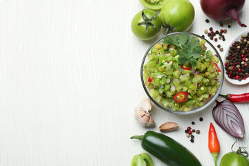 Tasty salsa in bowl and ingredients on white wooden table, flat lay. Space for text