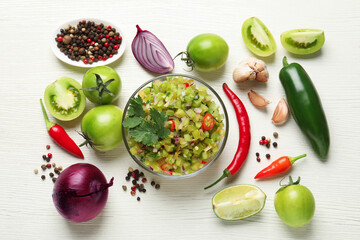 Tasty salsa in bowl and ingredients on white wooden table, flat lay