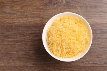 Grated cheese in bowl on wooden table, top view. Space for text