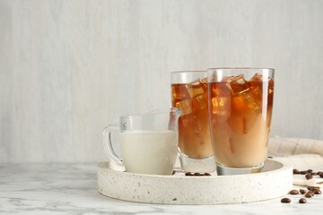 Tasty iced coffee with milk and beans on white marble table. Space for text