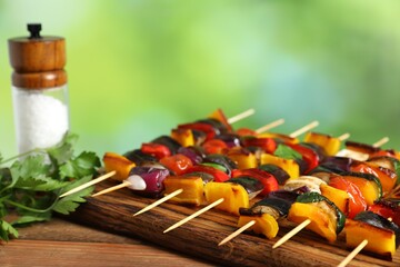 Skewers with tasty grilled vegetables and salt on wooden table against blurred background, closeup. Space for text