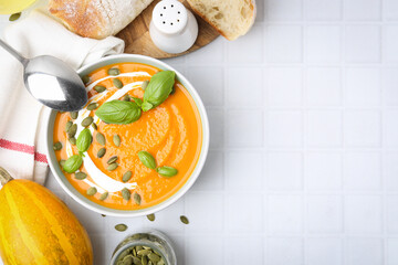 Delicious pumpkin soup served on white tiled table, flat lay. Space for text