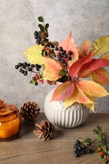 Autumn composition with vase of dry leaves, berries, pine cones and candle on wooden table near grey wall
