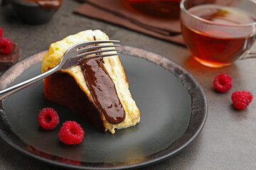 Piece of delicious Basque cheesecake with chocolate sauce, raspberries and tea on grey table, closeup