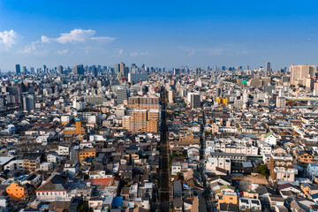 Fototapeta premium Aerial view of Osaka, Japan, in bright daytime. Low rise districts lead to modern towers. A straight railway divides the scene. Osaka Castle sits near mid right.