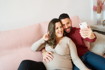 Happy pregnant couple taking selfie on sofa