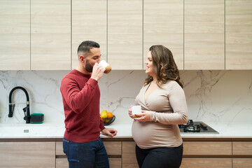 Pregnant couple talking, drinking coffee in kitchen