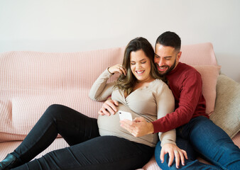 Expecting couple relaxing on couch using smartphone