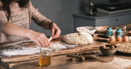 In a warm kitchen, a person prepares dough. They use flour to shape it on a wooden board,...