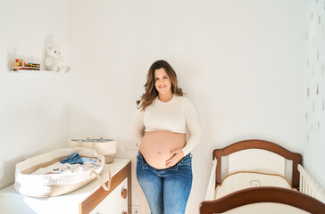 Expecting woman embracing baby bump in nursery