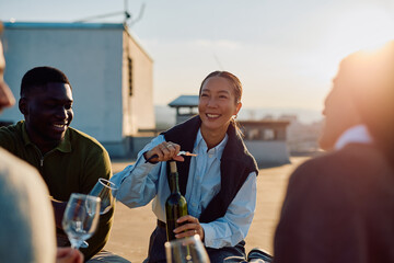Diverse friends celebrating on a rooftop, opening a bottle of wine and enjoying the golden hour together