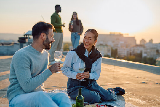 Diverse friends celebrating on a rooftop terrace during golden hour, sharing wine and food, enjoying urban city views
