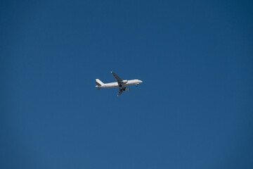 A white passenger plane flying low in the blue sky, landing or taking off. The concept of travel, transportation, and air travel.