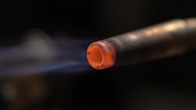 Closeup of a metal torch nozzle glowing red with blue flame