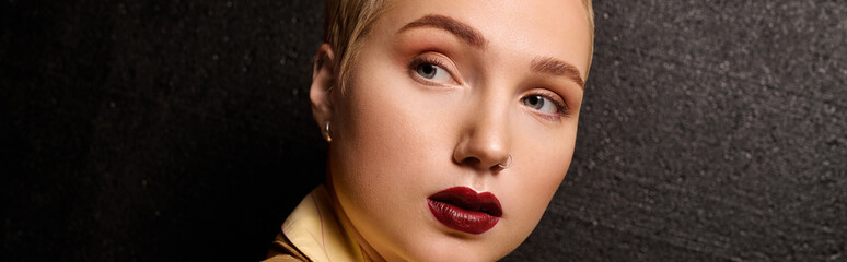 Fashionable young woman with bold makeup poses elegantly against a textured dark backdrop